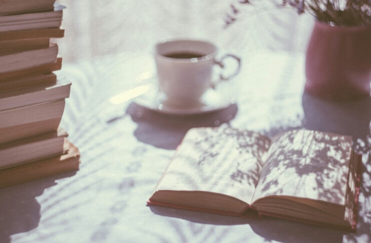 Otwarta książka, w tle filiżanka kawy, obok stos książek